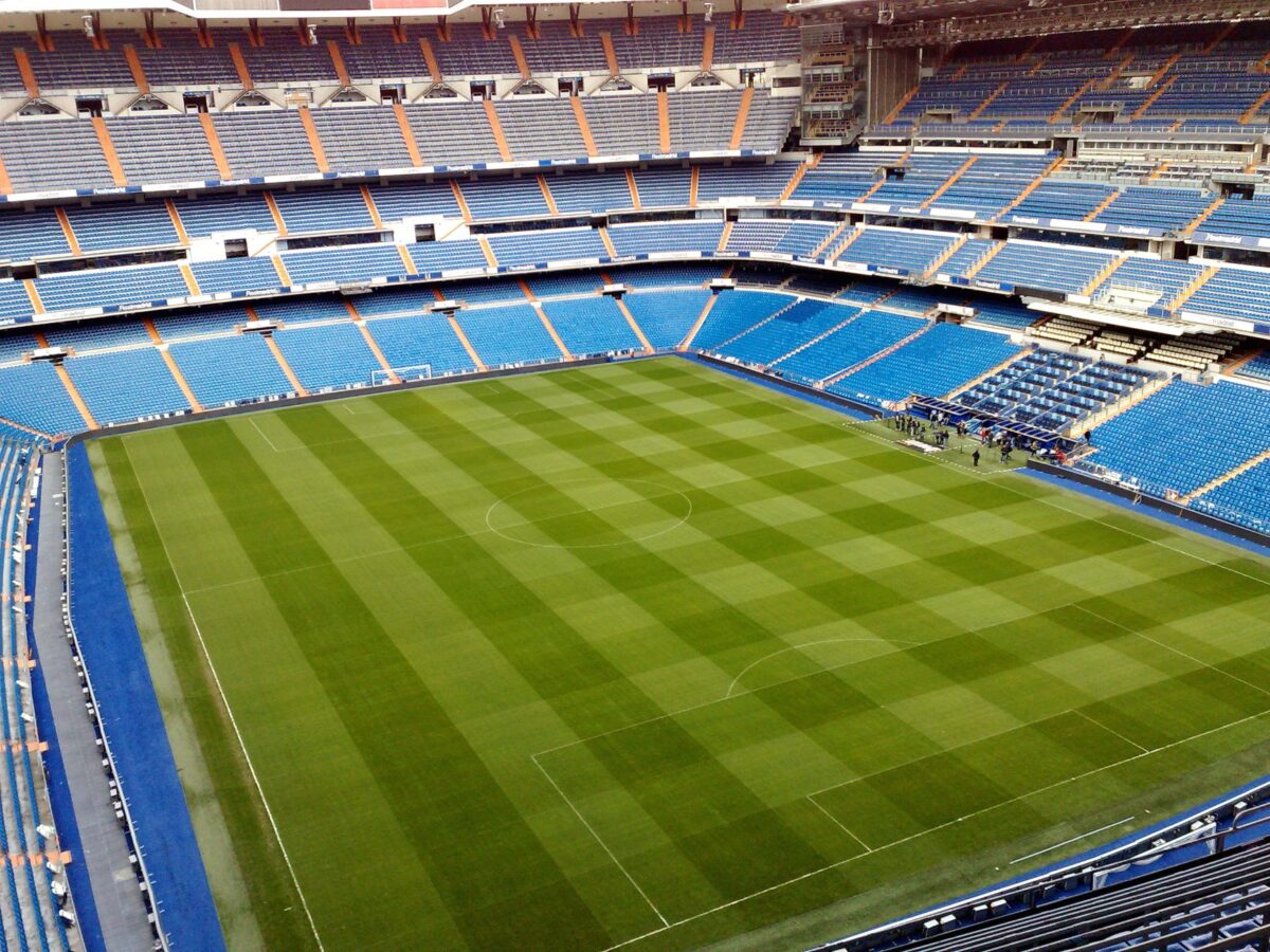 Aerial view of an empty soccer stadium with neatly trimmed green field and blue seating arrangements.